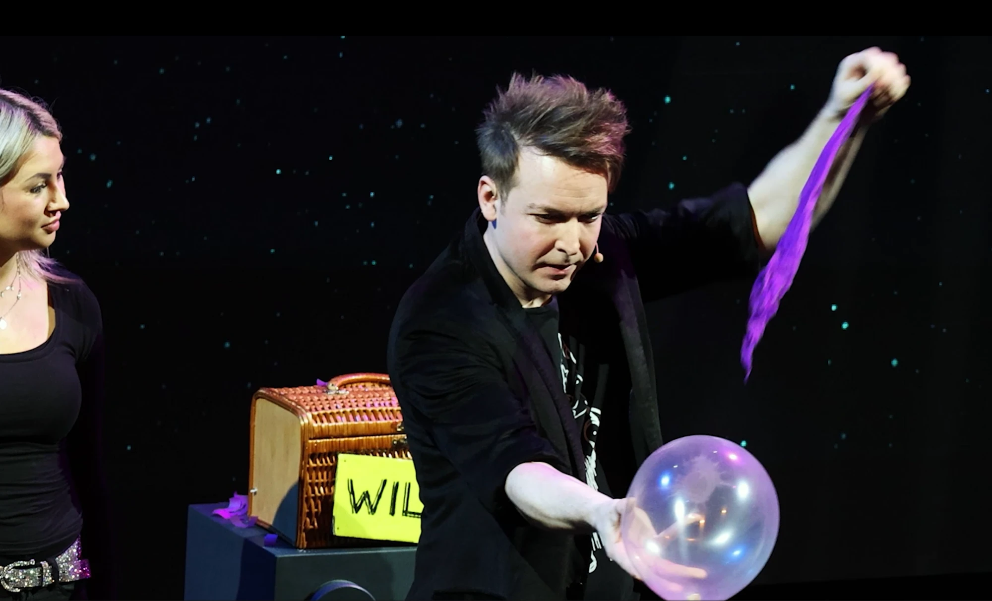 Florian Zimmer zieht ein lila Tuch aus einem durchsichtigen Luftballon